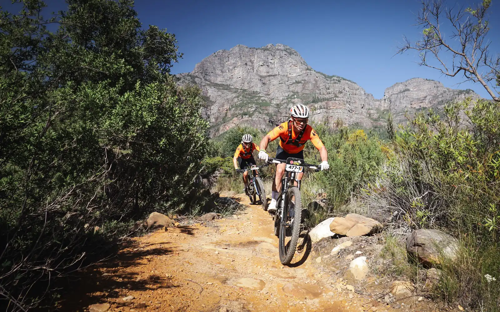 Hyperclear MTB Racing Team cyclists navigating a technical mountain trail during the Absa Cape Epic for Raise for a Child.