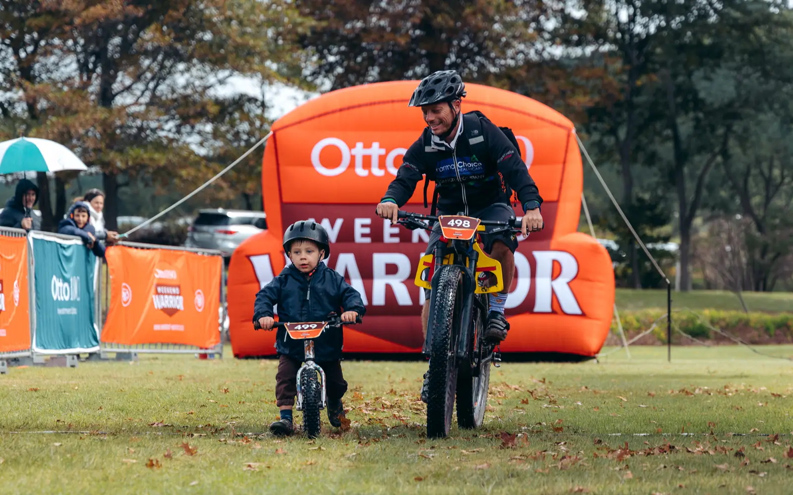 Hyperclear mentor and young mountain bikers in orange jerseys riding a dusty scrubland trail during a Weekend Warrior adventure for Raise for a Child.